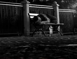 man in black shirt sleeping on brown wooden bench during daytime thumbnail