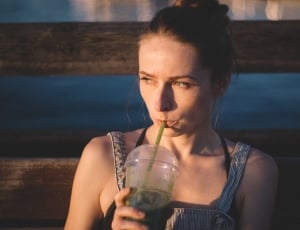woman in grey sleeveless top holding disposable cup near brown wooden wall thumbnail