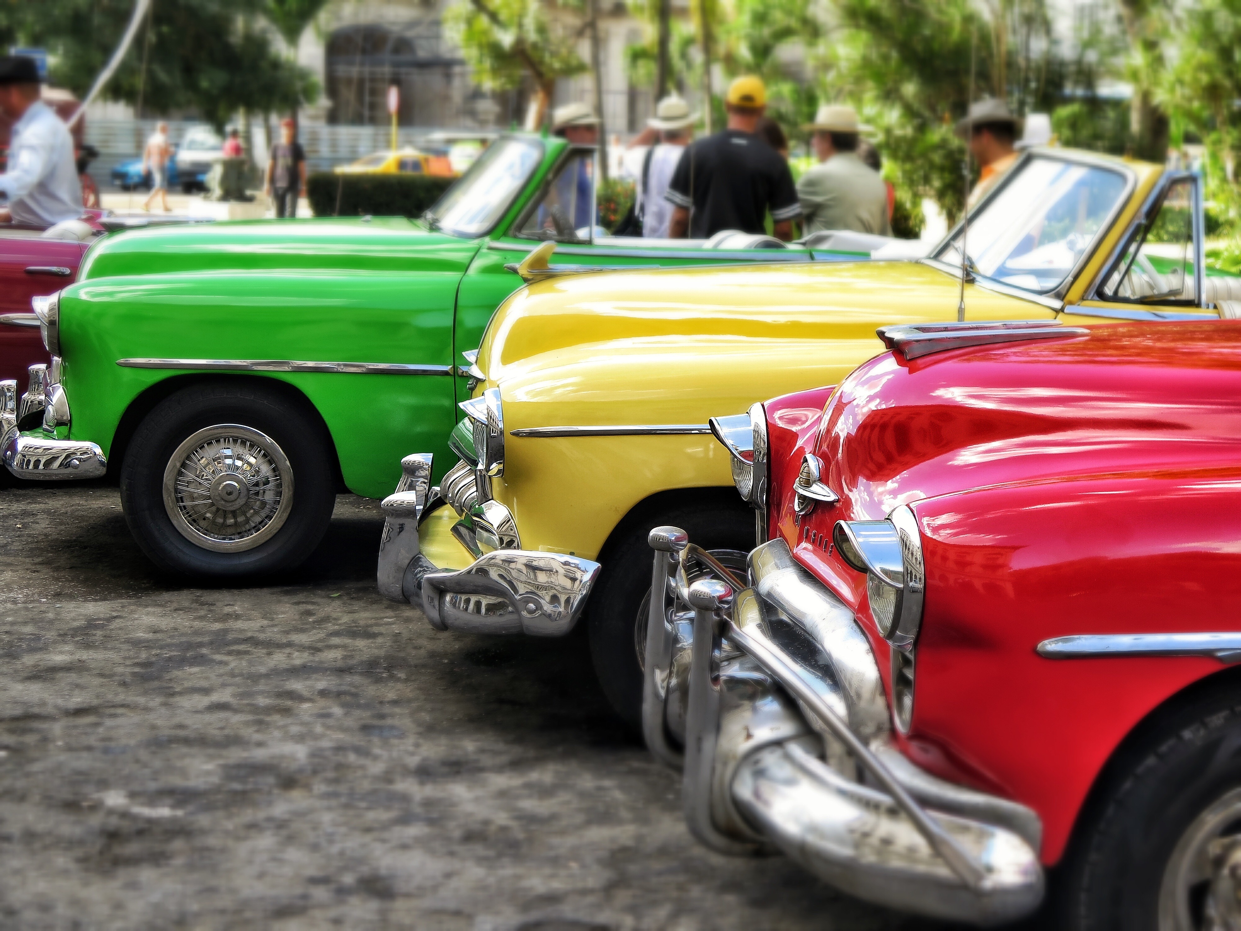three red, yellow and green classic cars in parked near people at daytime