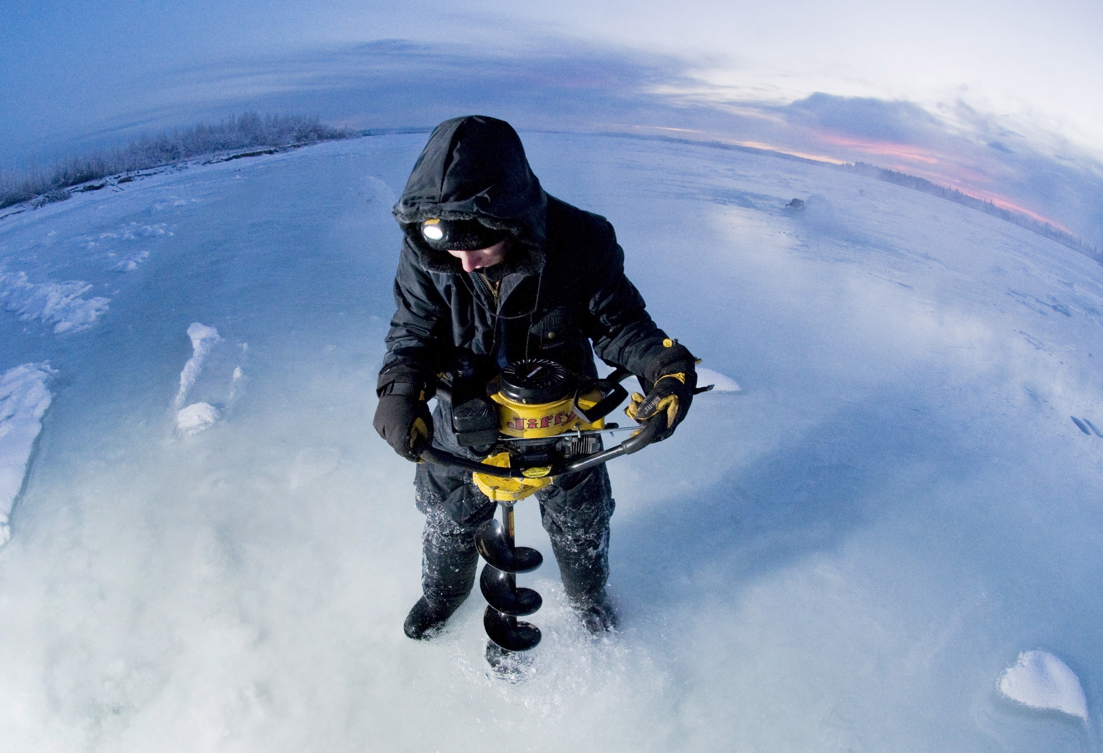 man wearing black jacket while using ice auger to pierce ice floor