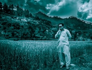man in long sleeve top and pants and trek sandals outfit standing beside field at daytime thumbnail