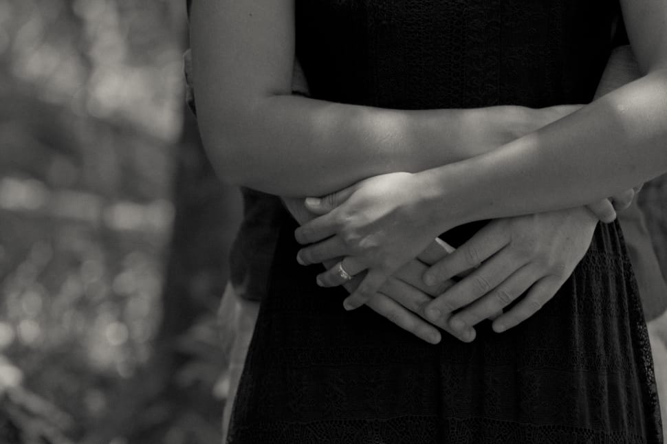 grayscale photo of person hugging woman wearing dress from the back preview
