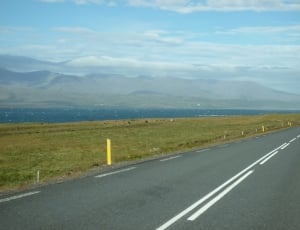 photo of gray concrete road, green grass field and mountain during daytime thumbnail