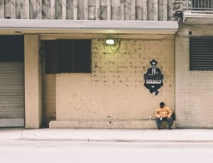Man in Yellow Jacket Sitting on White Waiting Shed thumbnail
