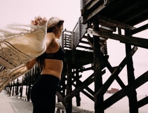woman in black sports bra holding brown and black scarf near brown wooden bridge during daytime thumbnail
