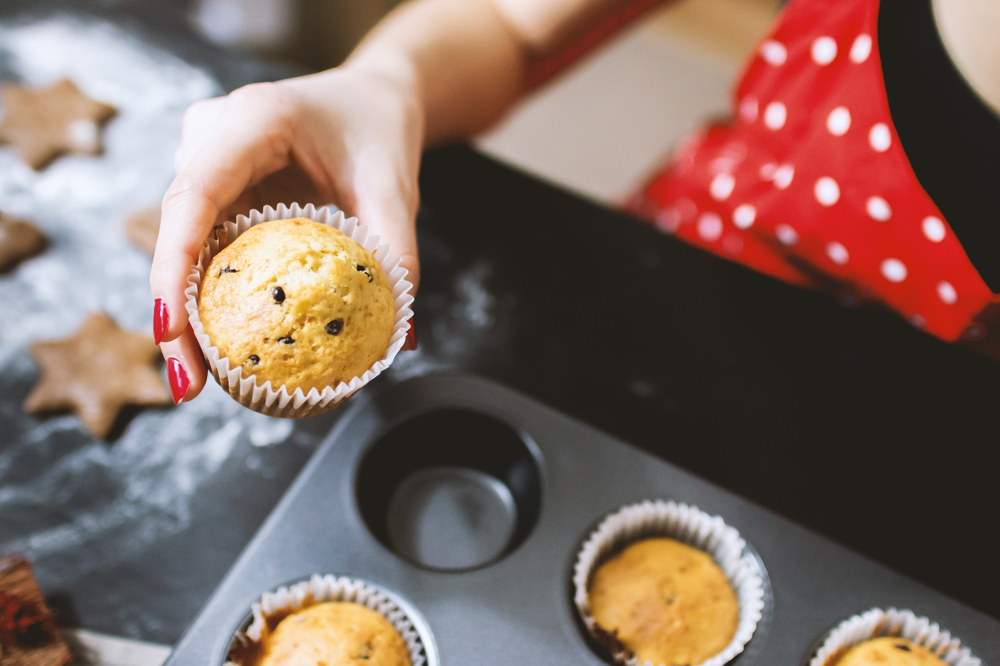 woman wearing red manicure holding muffin from baking pan