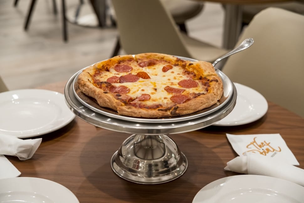 pizza on stainless steel pedestal tray on brown wooden round dining table preview