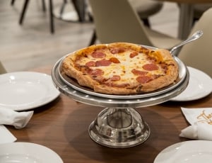 pizza on stainless steel pedestal tray on brown wooden round dining table thumbnail