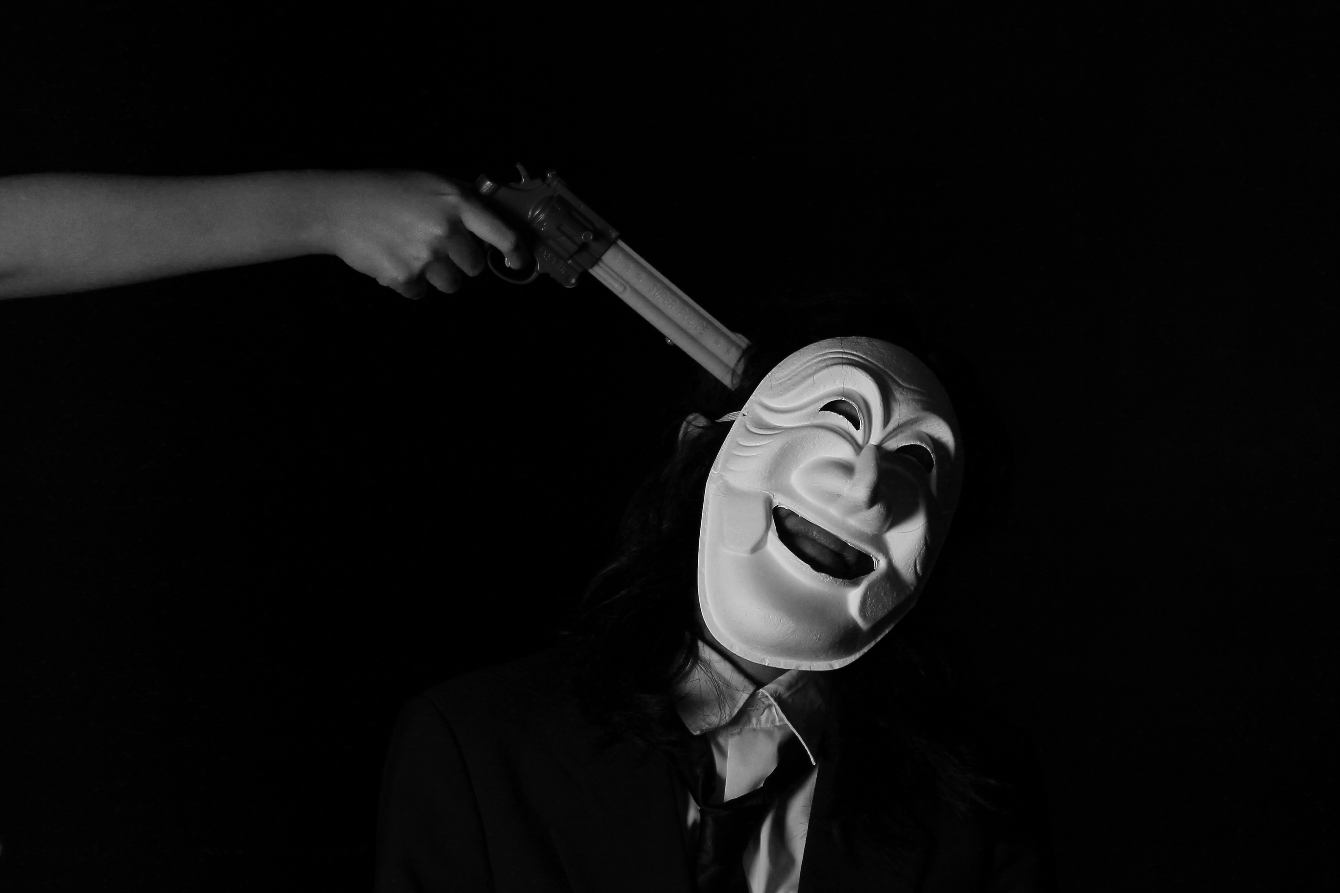 man in white mask wearing black necktie with gun pointed on his head