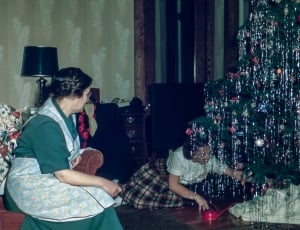 girl decorating the christmas tree while the woman sitting on a chair watching her thumbnail