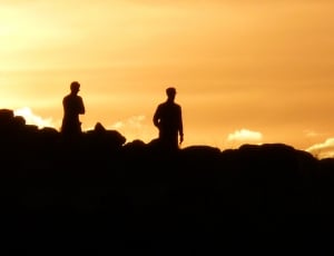 silhouette of two person standing on hills during golden hour thumbnail