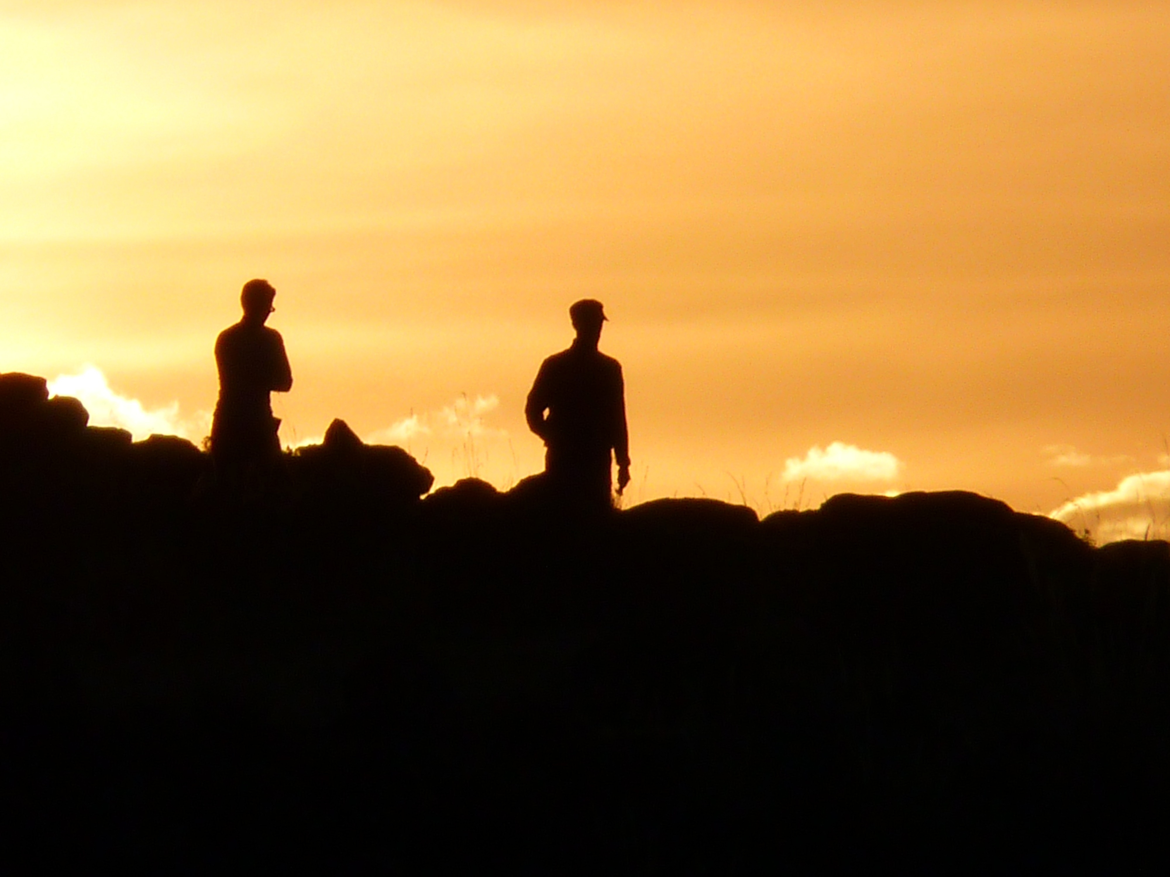 silhouette of two person standing on hills during golden hour