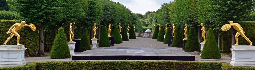 green cone shaped bushes with man gold staTUES preview