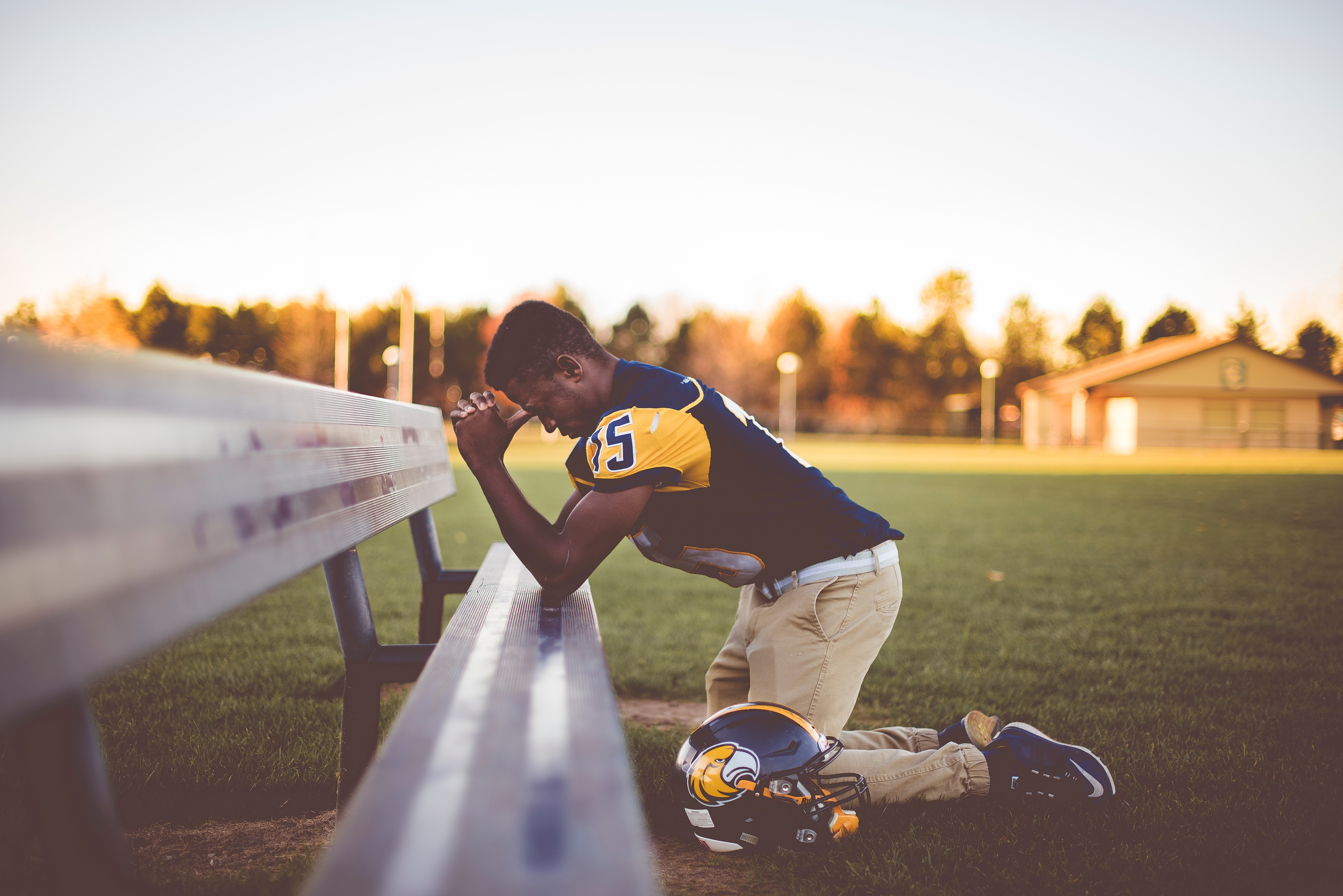 football player kneeling before bench on green field praying