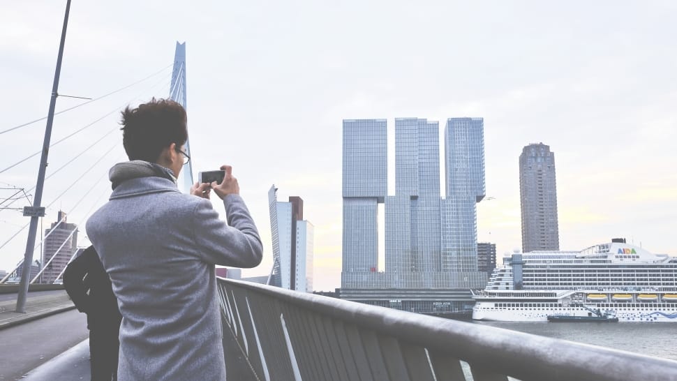 person wearing gray coat holding a camera taking a photo of buildings preview