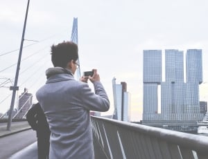 person wearing gray coat holding a camera taking a photo of buildings thumbnail