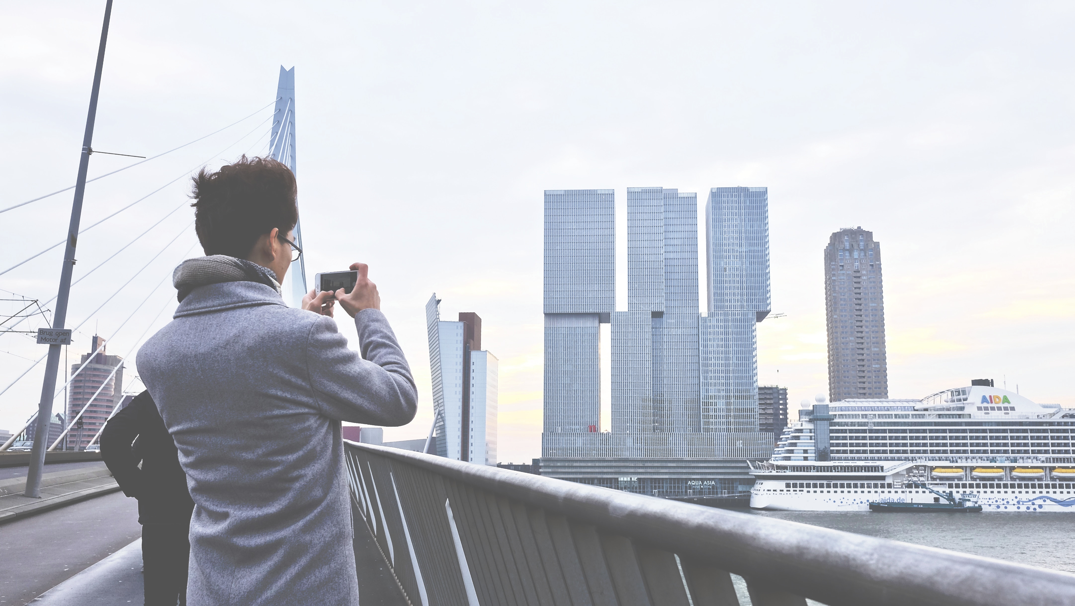 person wearing gray coat holding a camera taking a photo of buildings