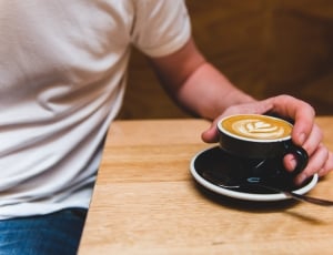 men's holding cappuccino on brown wooden table inside room thumbnail
