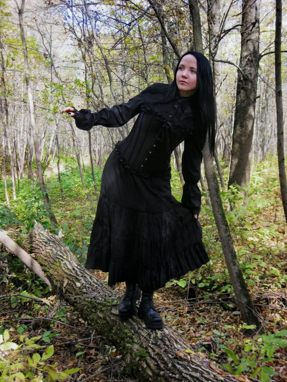 woman in black long sleeve button-up long dress and black leather boots standing on wood tree branch under green leaf tree during daytime preview