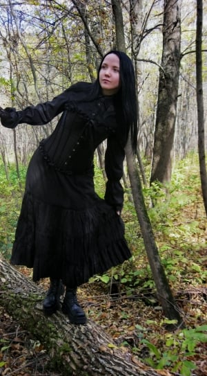 woman in black long sleeve button-up long dress and black leather boots standing on wood tree branch under green leaf tree during daytime thumbnail