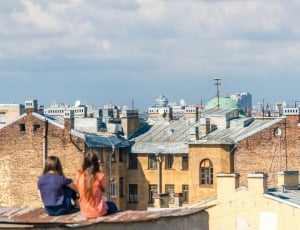 two women sitting on the roof looking at the houses thumbnail