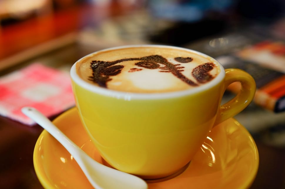 cat foam art latte on brown ceramic cup on saucer and white teaspoon preview
