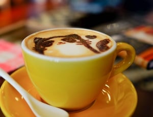 cat foam art latte on brown ceramic cup on saucer and white teaspoon thumbnail