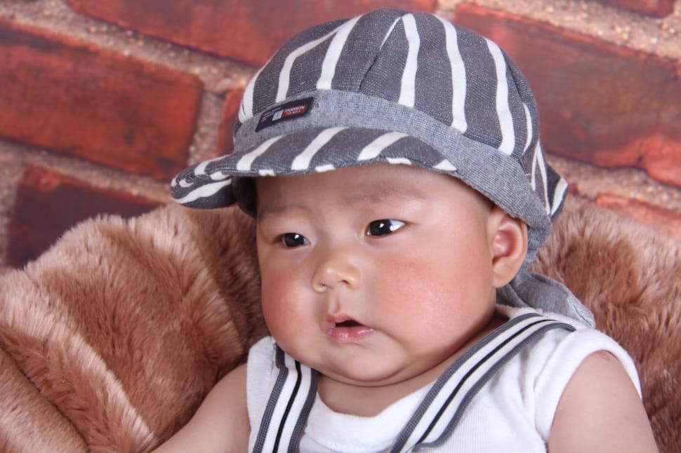 baby boy in white tank top and gray hat sitting on chair preview