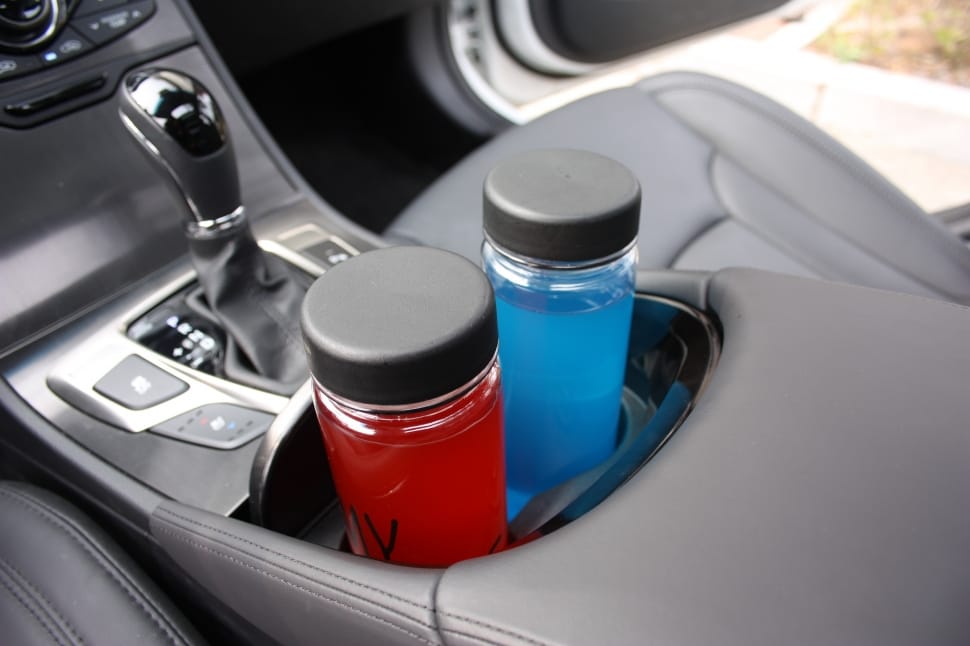 two clear glass with black lids bottles on car near gear shift lever preview