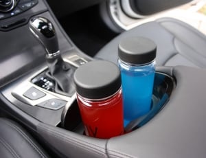 two clear glass with black lids bottles on car near gear shift lever thumbnail