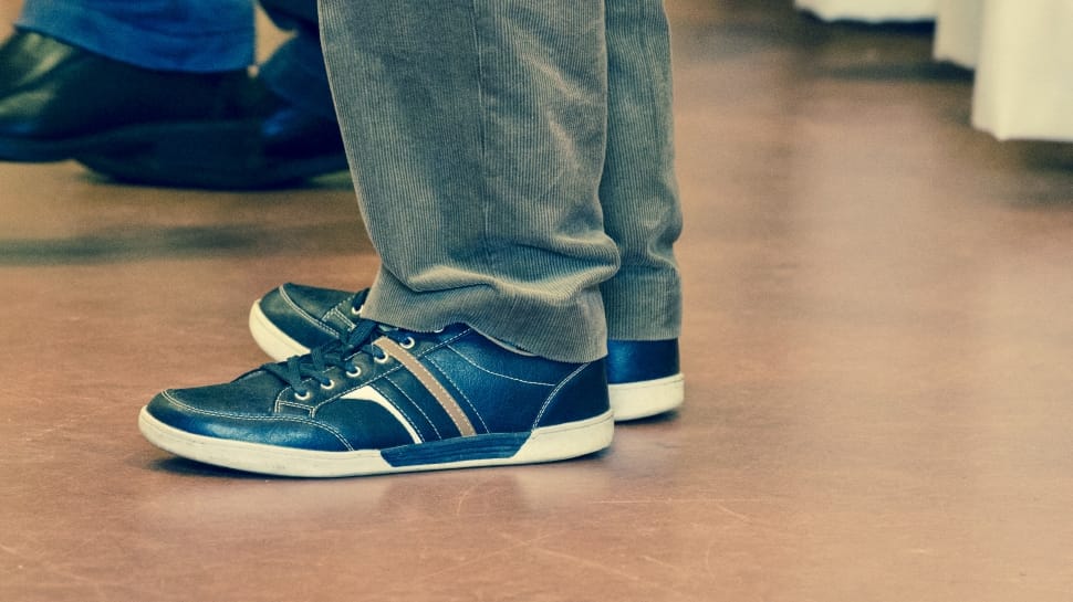 person wearing blue-and-white low top sneakers and blue denim jeans standing on brown floor tile preview