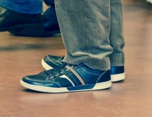 person wearing blue-and-white low top sneakers and blue denim jeans standing on brown floor tile thumbnail