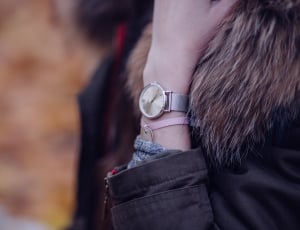 person wearing black-and-brown fur coat with pink bracelet and silver analog watch in left arm thumbnail