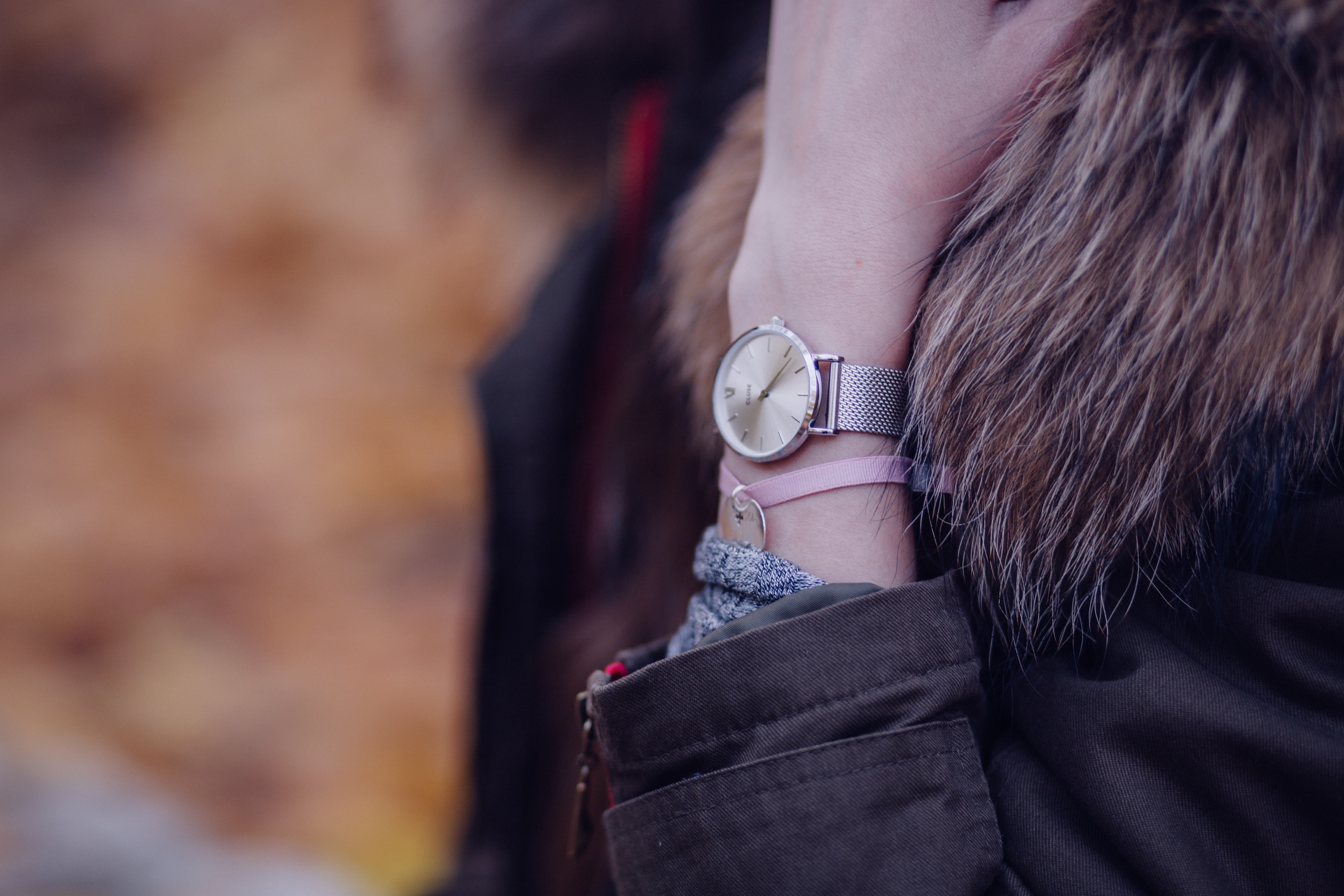 person wearing black-and-brown fur coat with pink bracelet and silver analog watch in left arm