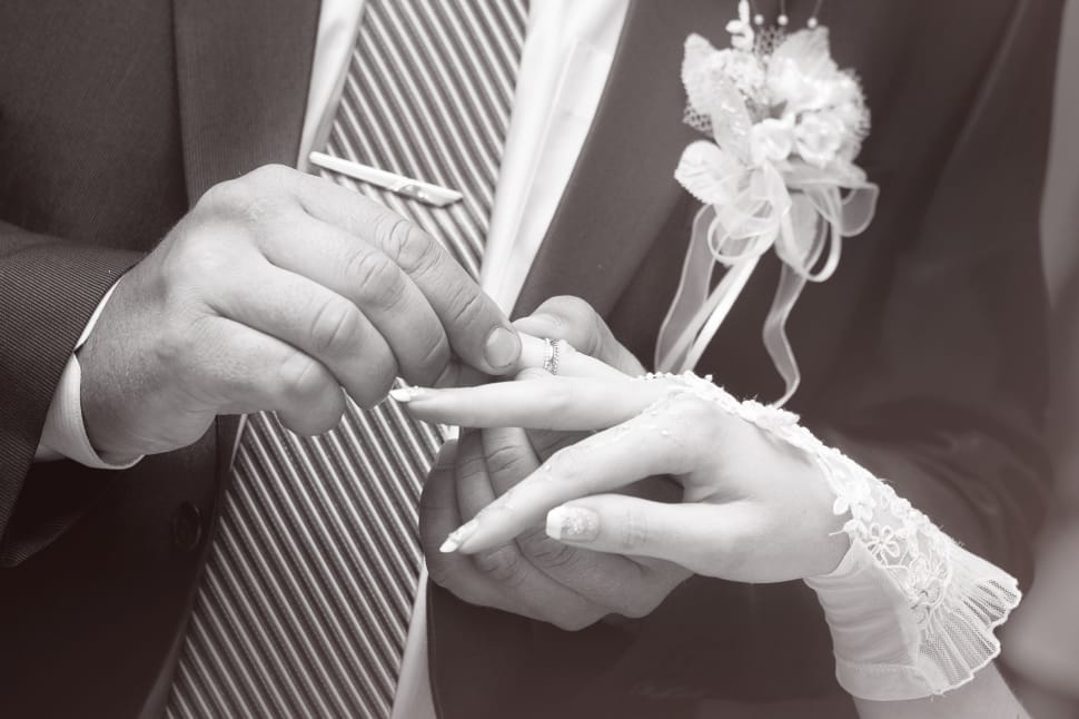 gray scale photo of groom placing the ring to his bride preview