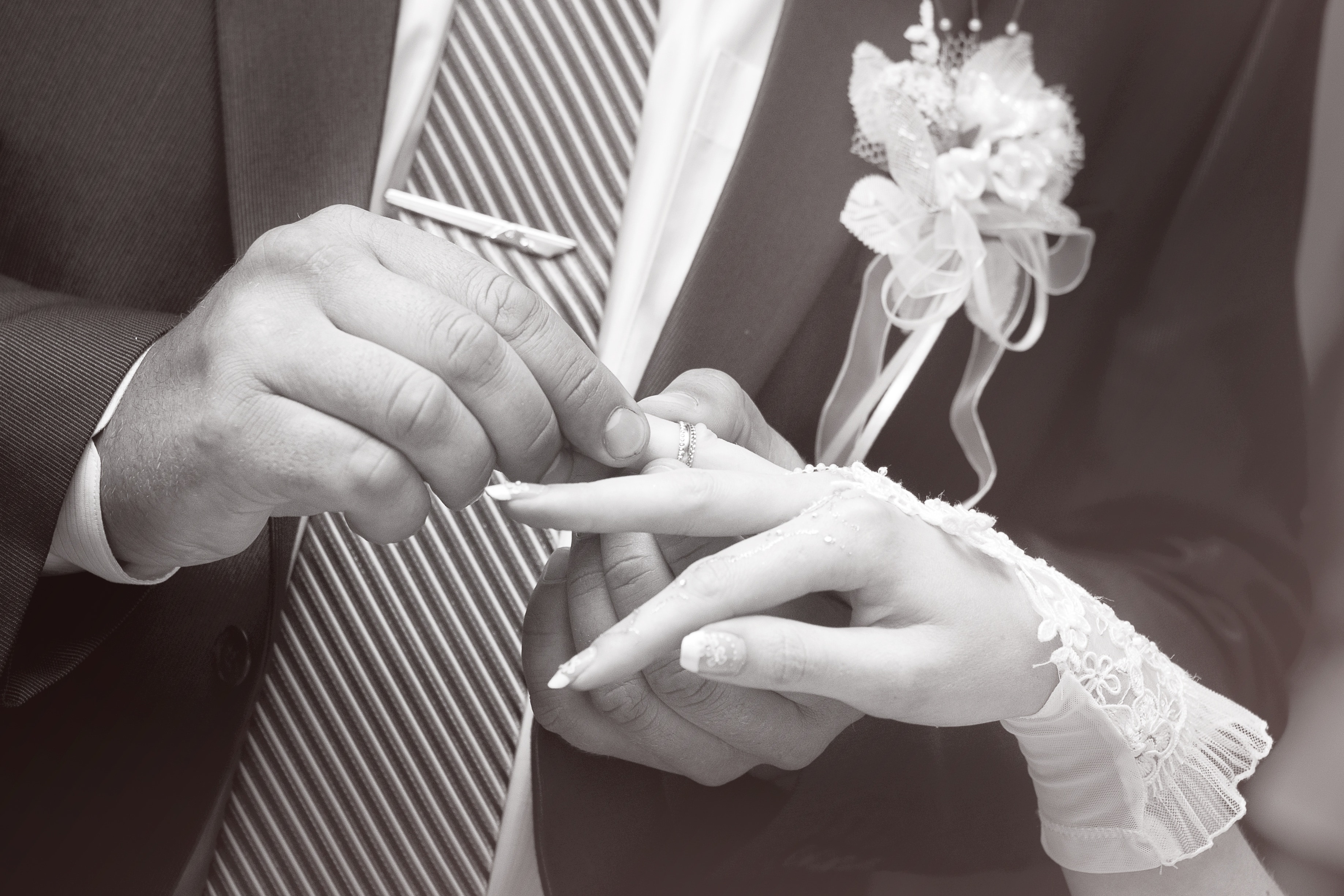 gray scale photo of groom placing the ring to his bride