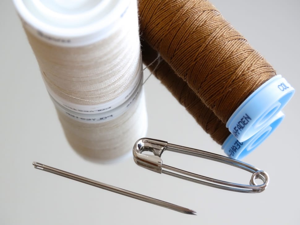 two white and brown sewing threads, needle and safety pin preview