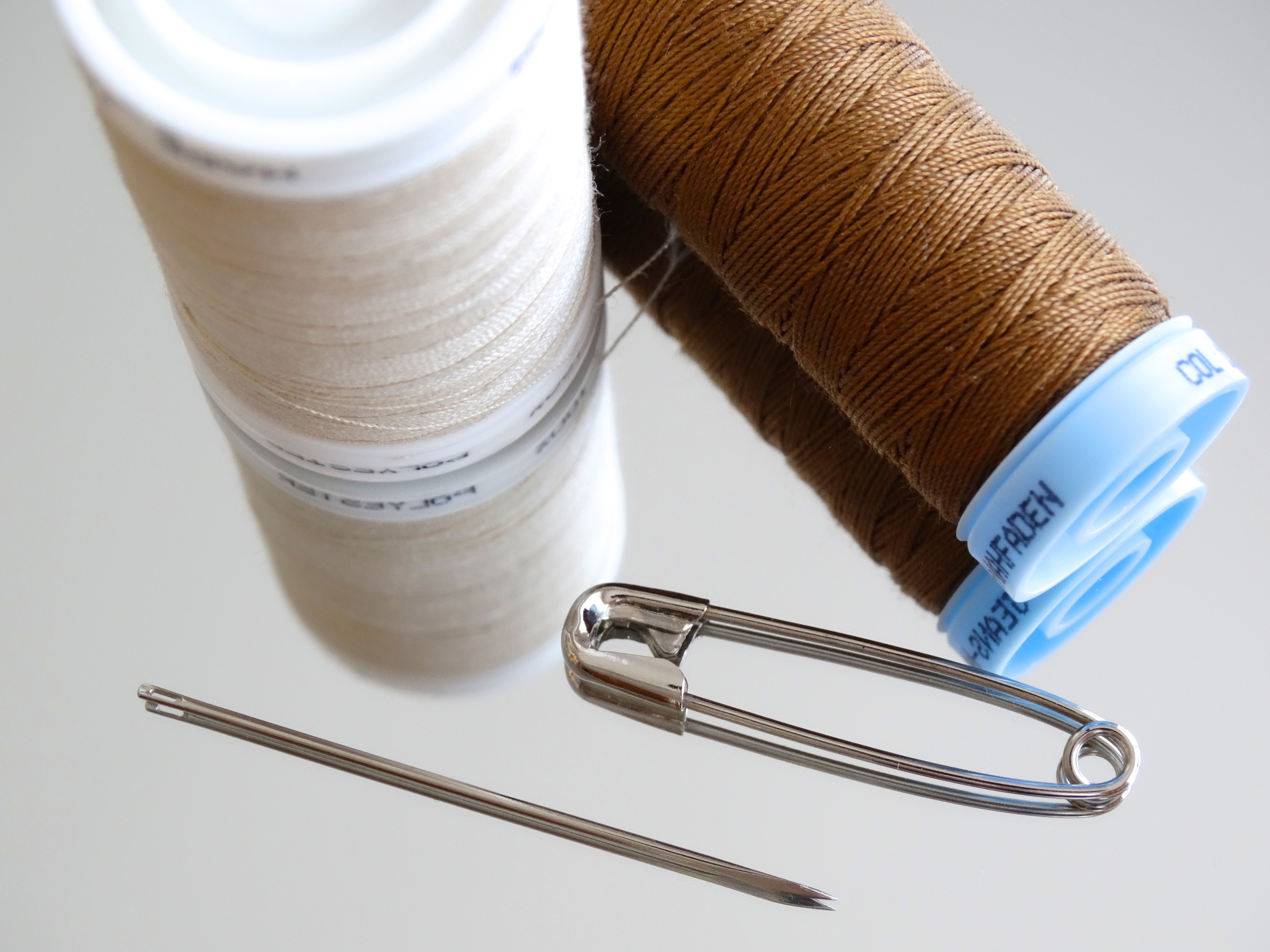 two white and brown sewing threads, needle and safety pin