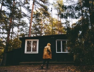 person wearing brown hoodie standing near cabin during daytime thumbnail