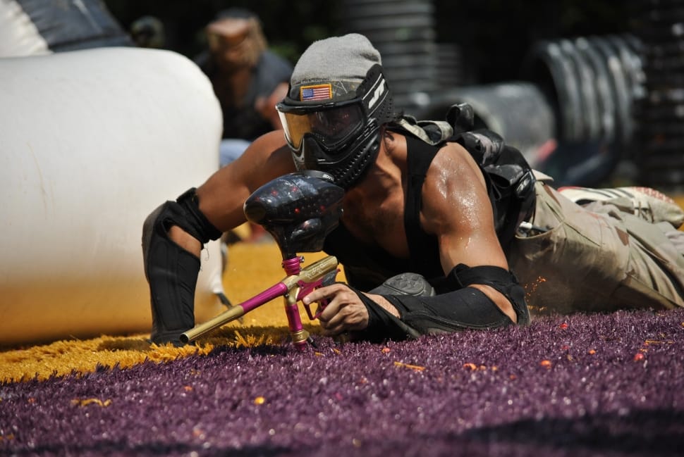 man wearing a black paintball gear holding a black,gold, and pink paintball gun preview