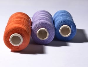 three orange, purple, blue rolled threads on white background thumbnail