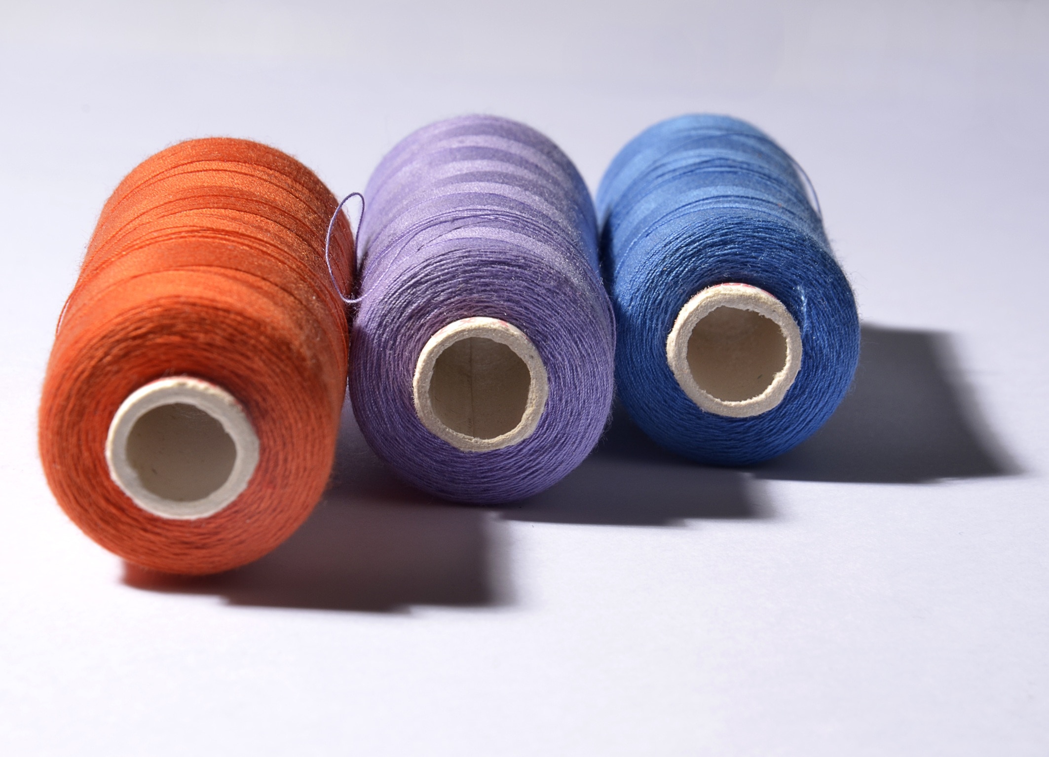 three orange, purple, blue rolled threads on white background