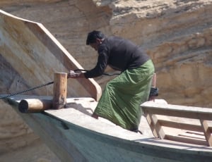 man tying rope on pole of wooden boat thumbnail