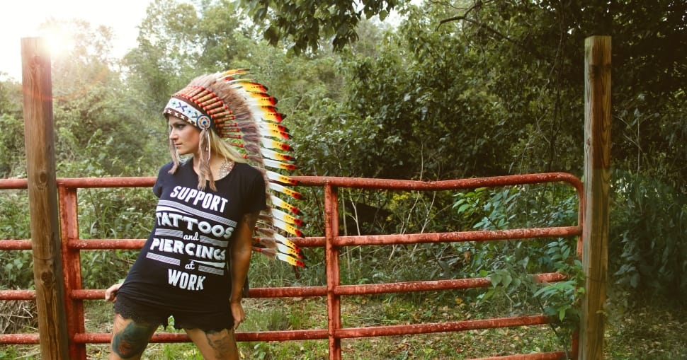 woman standing near fence with Native American head dress preview