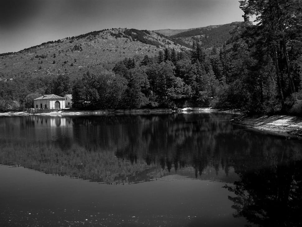 grayscale photography of house near body of water under mountain during daytime preview