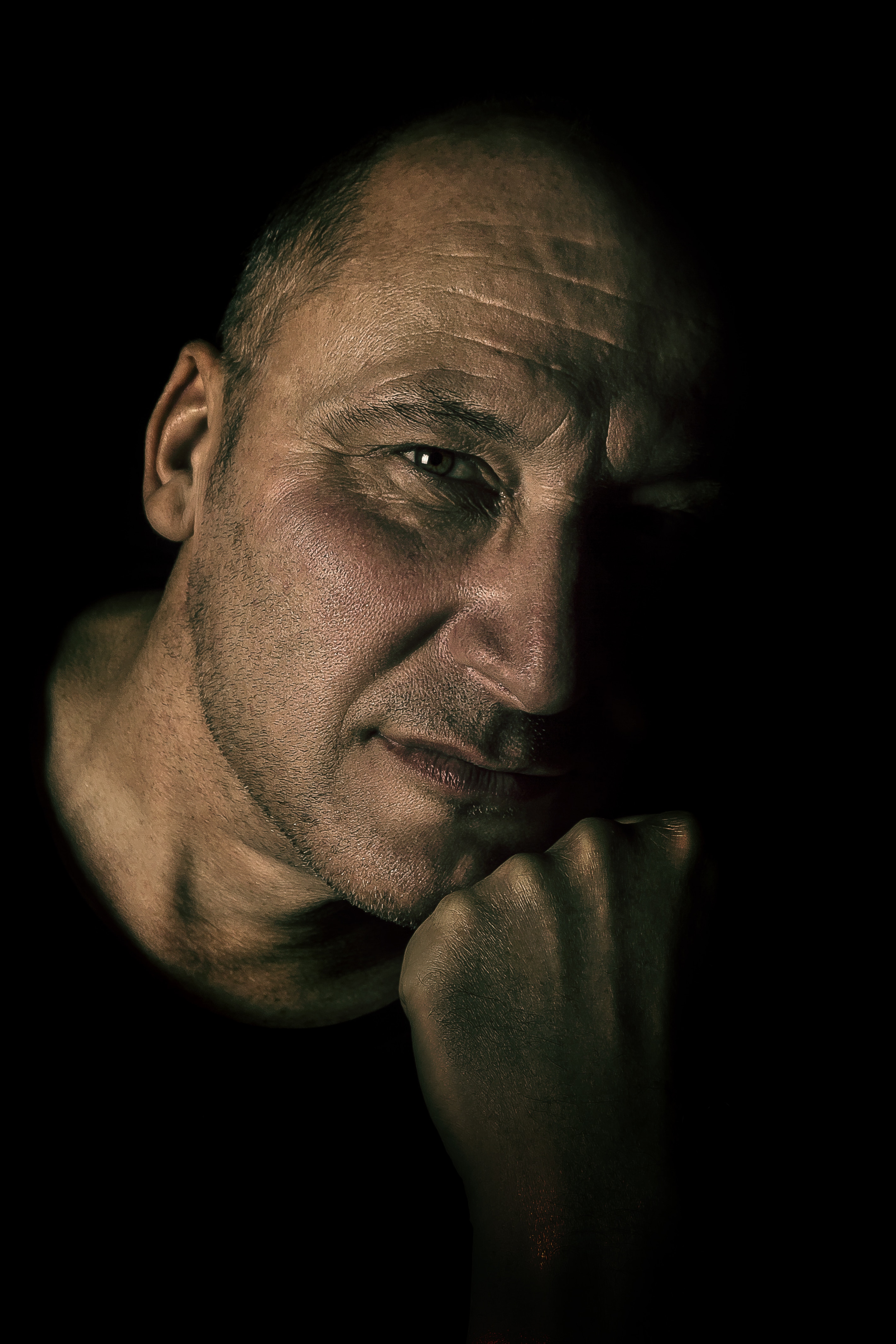 man in black t shirt leaning on his arm in dark background