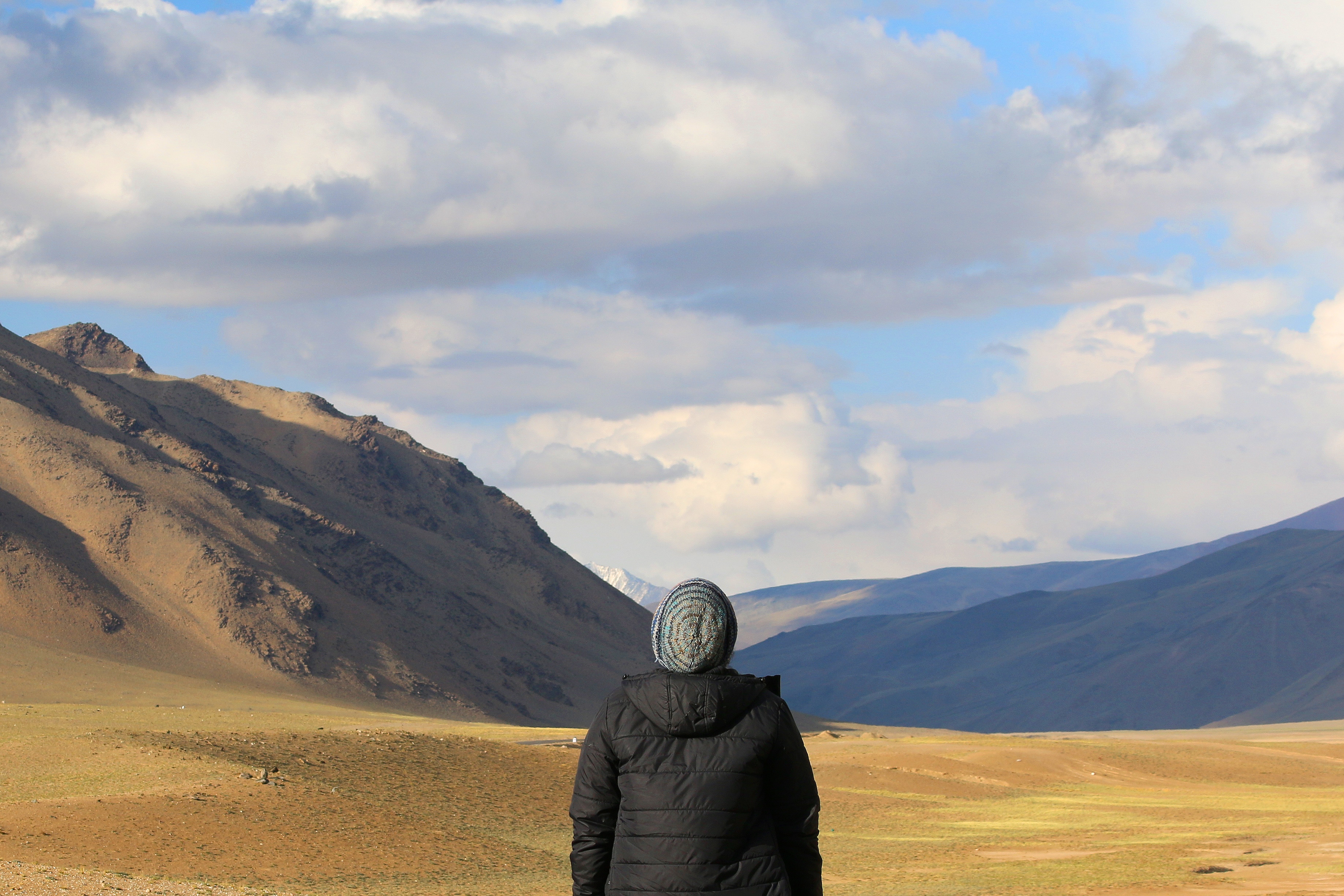 person in black bubble hoodie wearing grey knit cap standing on brown dirt road near rock formation during daytime