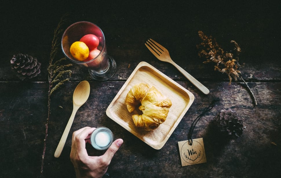 person holding gray tool with croissant and spoon and fork preview