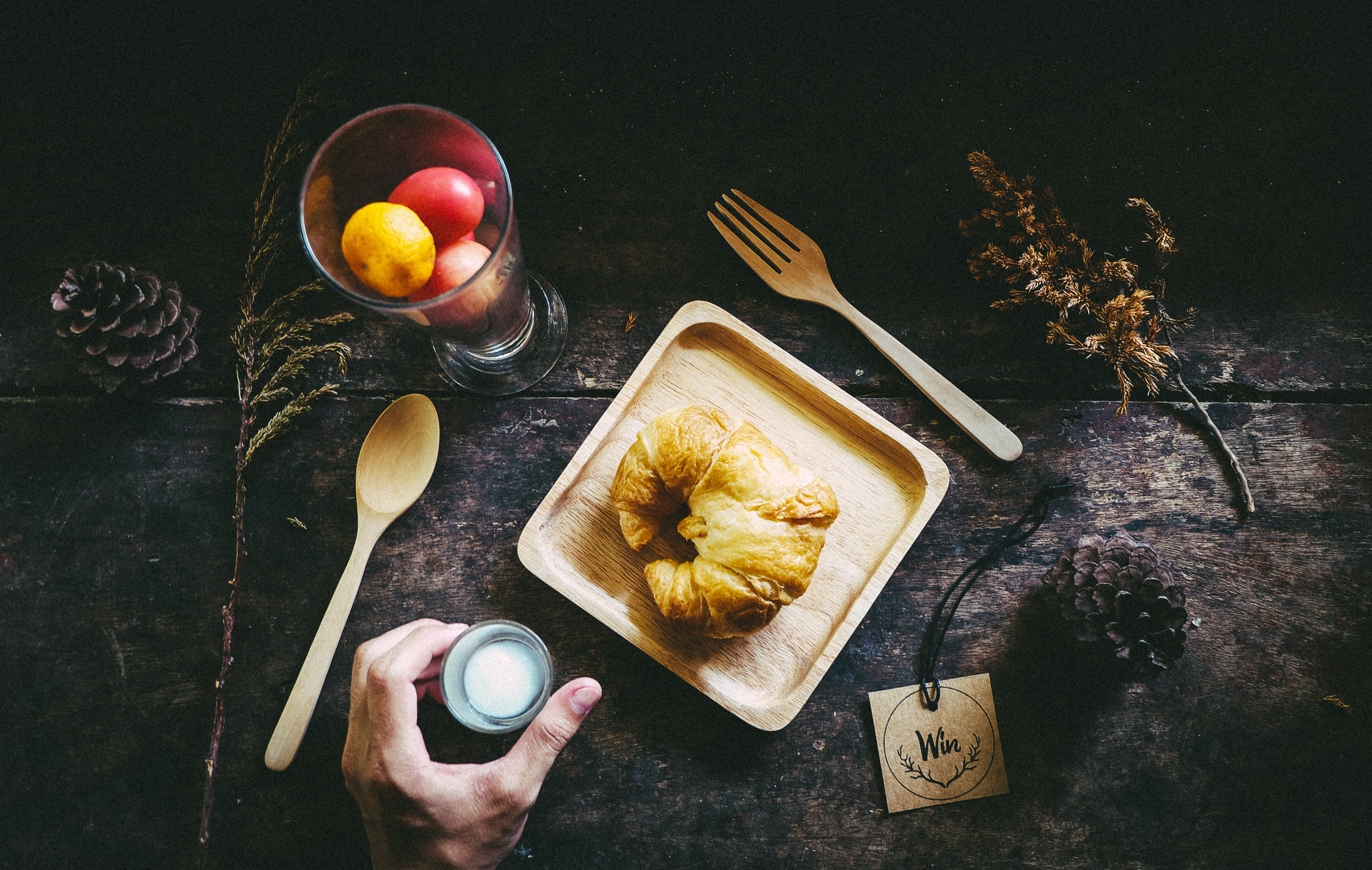 person holding gray tool with croissant and spoon and fork
