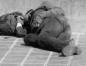 photo of person in long sleeve and jeans with shoes near backpack lying on pavement in gray-scale photography thumbnail